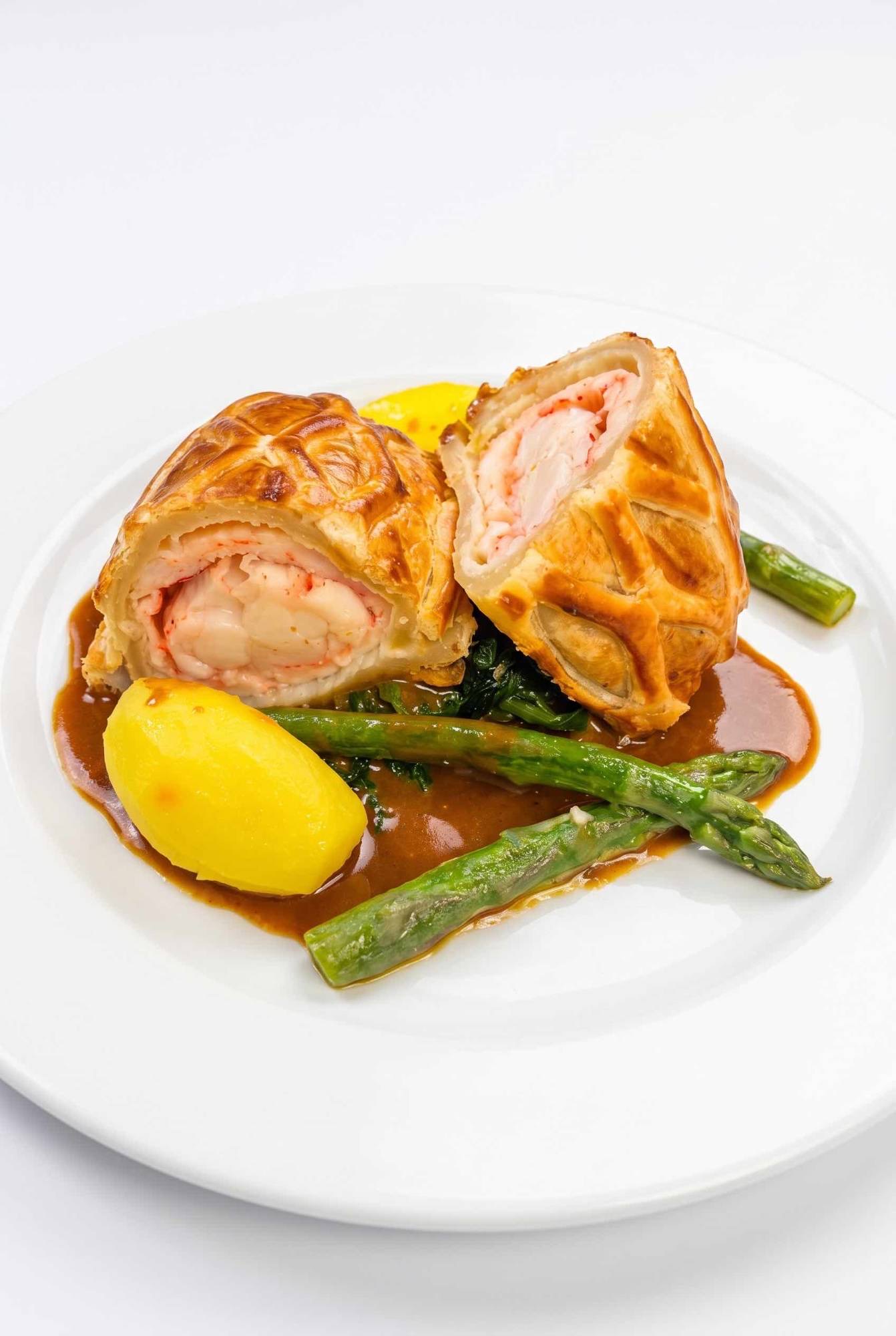Lobster Wellington cut in half, with asparagus, wilted greens, a buttered potato and a rich sauce