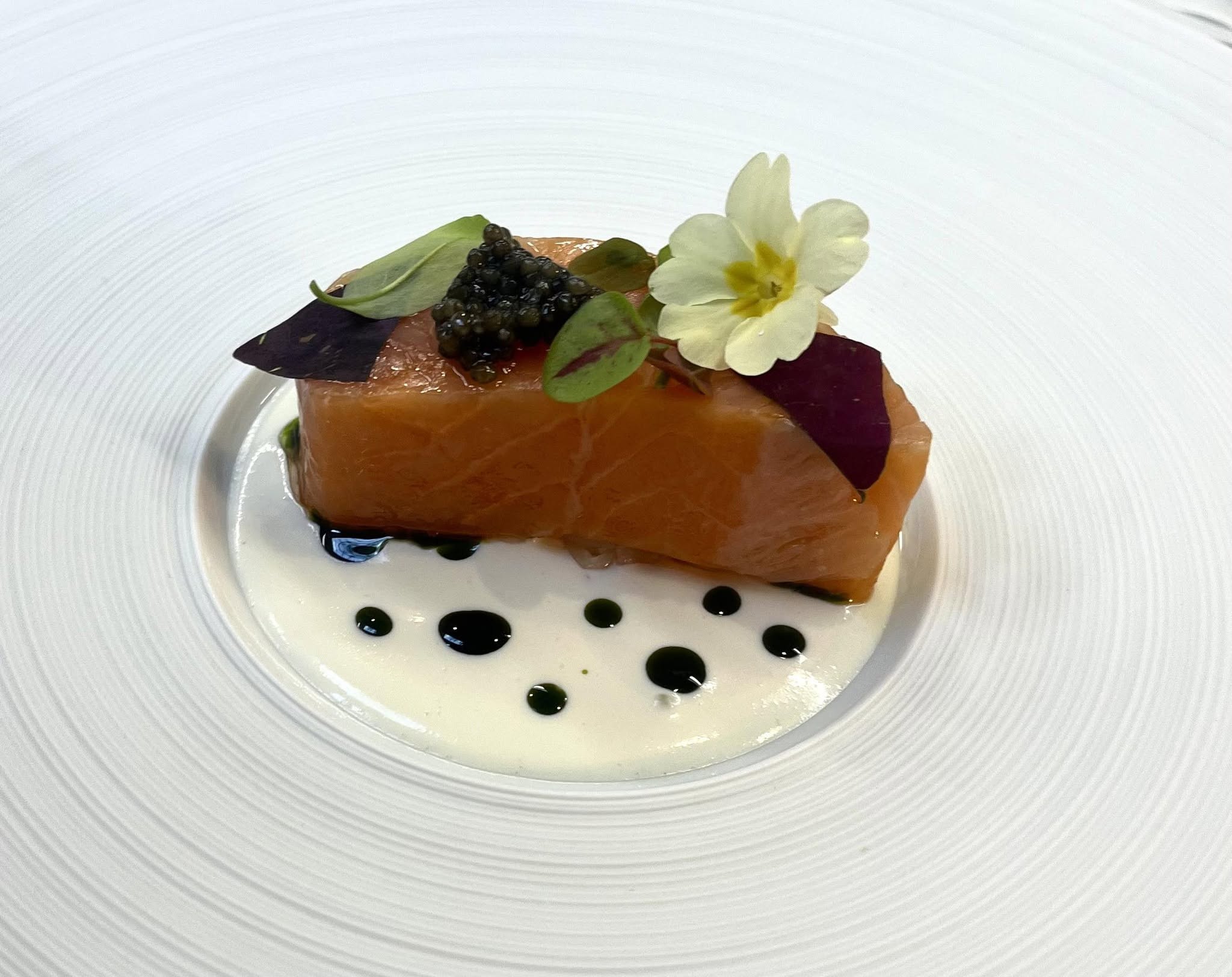 Cured salmon with caviar, micro herbs and a primrose flower on a crème fraîche sauce