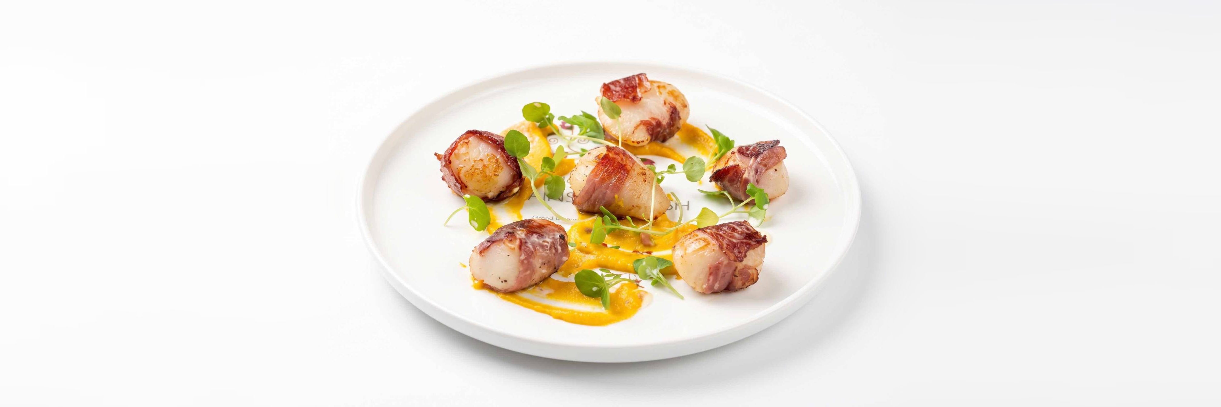 Seared scallops wrapped in Parma ham on a golden purée, scattered with pea shoots
