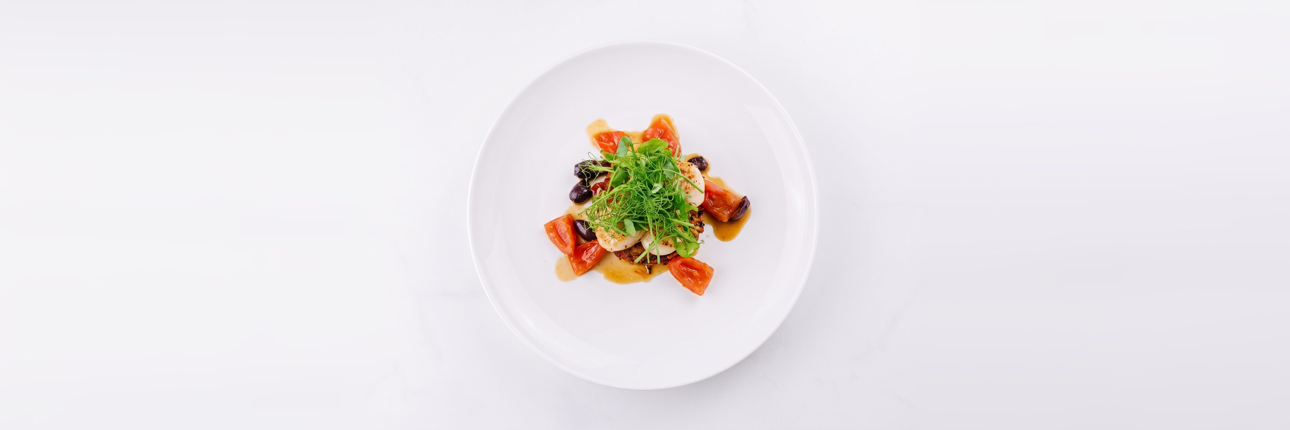 Seared scallops with pea shoots, tomato, black olives and a butter sauce, seen from above