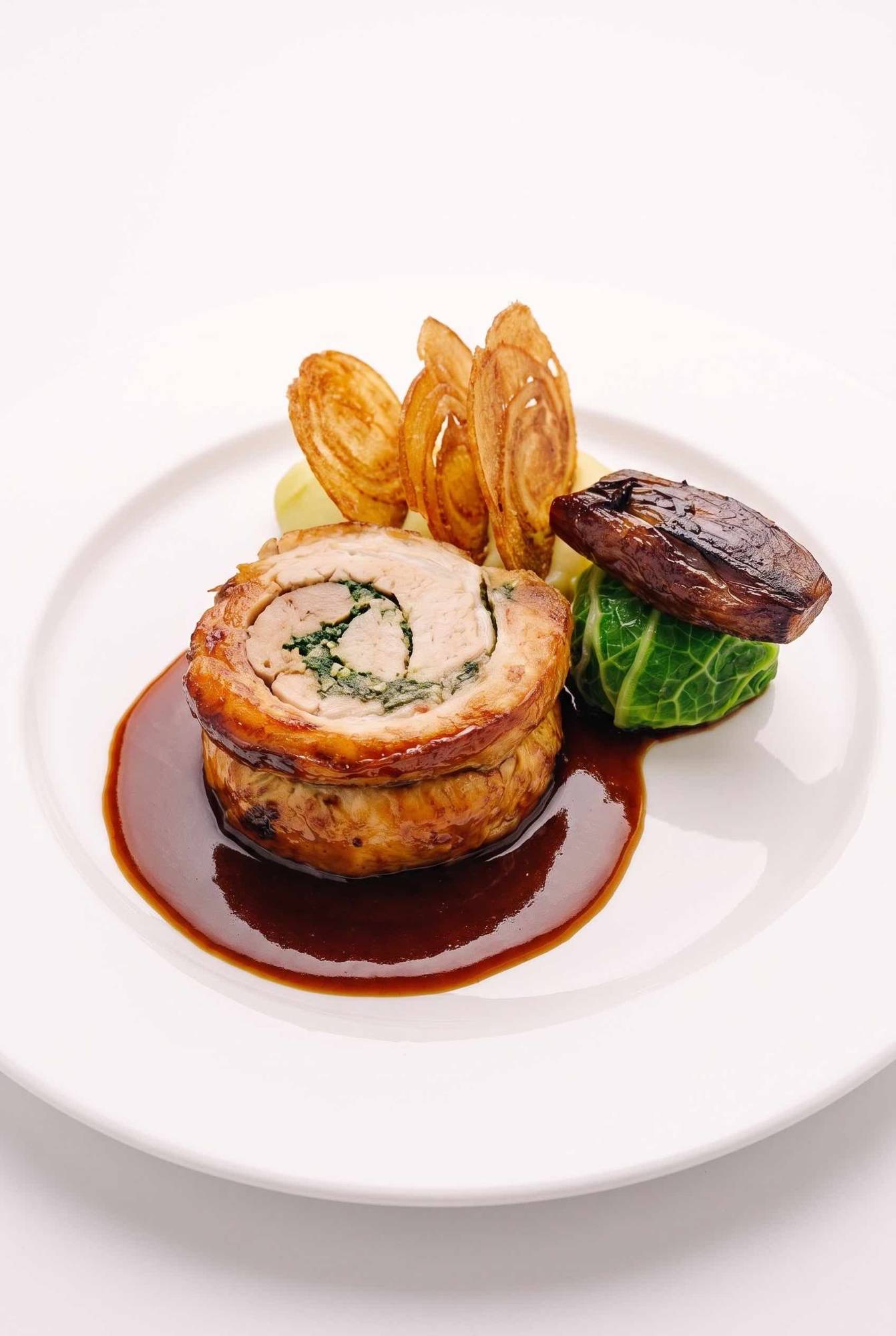 A roulade of meat rolled around a spinach stuffing, with crisp onion slices, mash, a Savoy cabbage parcel, a roasted shallot and a glossy jus