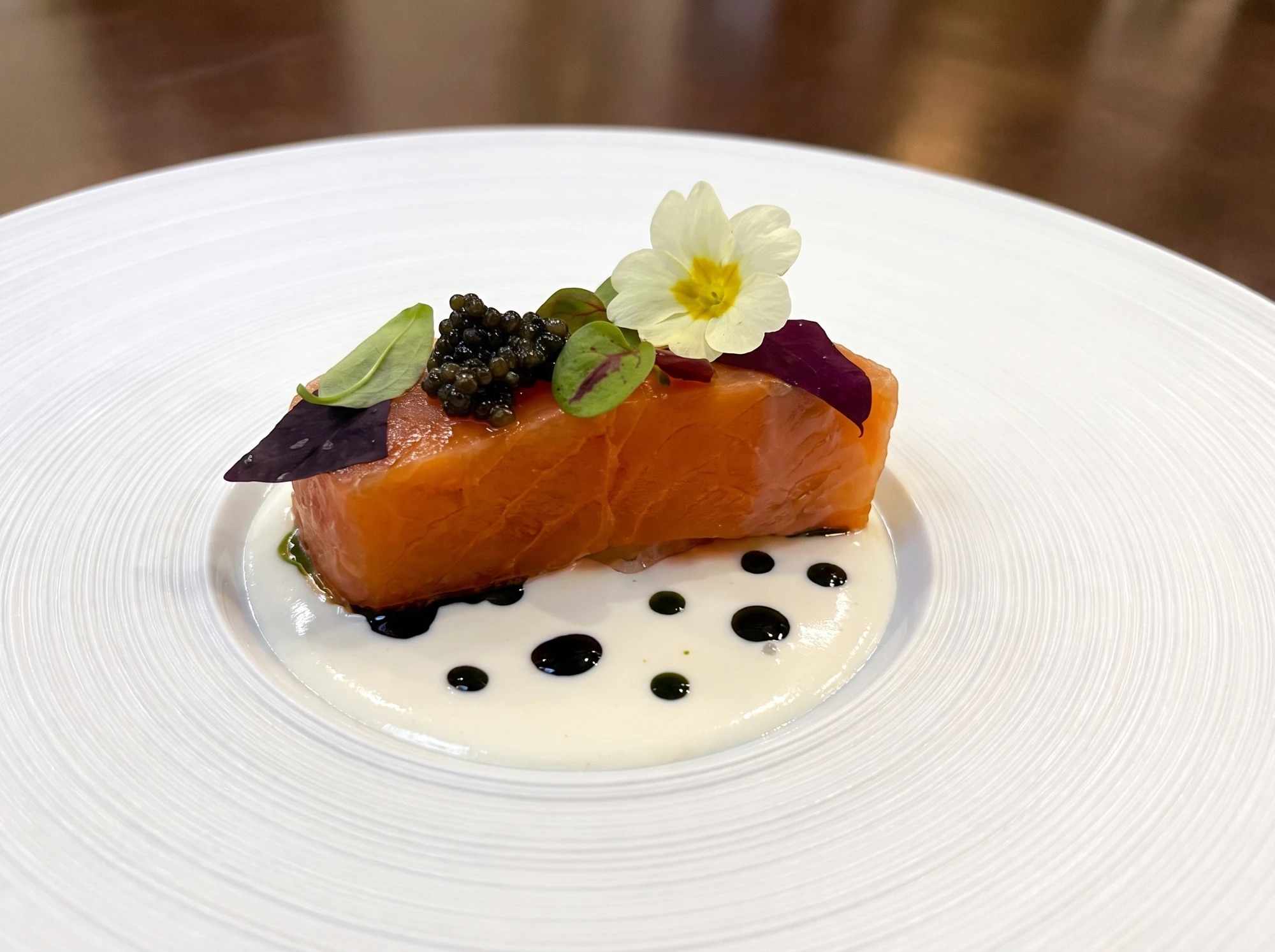 Cured salmon with caviar, micro herbs and a primrose flower on a crème fraîche sauce